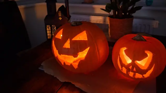Two carved pumpkins sit on a table at night.
