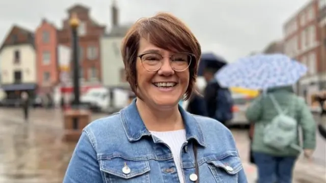 A woman with short red hair and a blue denim jacket