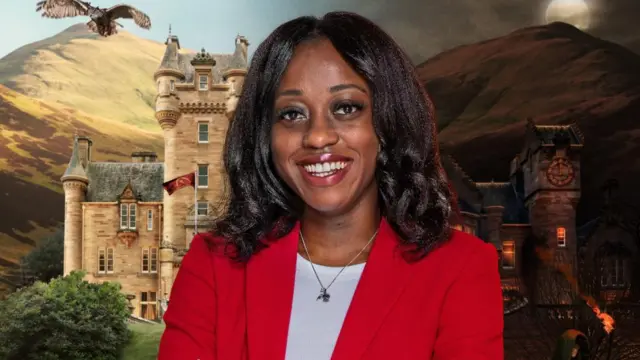 Minah Shannon, wearing a red blazer, smiling in front of a picture of a castle