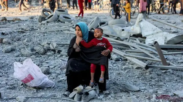 A woman child sit among grey rubble, pensively.