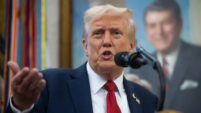 Close up of Donald Trump mid-speech. He's in a dark blue suit and red tie, behind him, affixed to the wall, is an oil painting of former US President Ronald Reagan