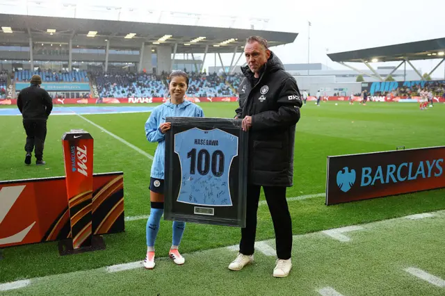 Yui Hasegawa of Manchester City poses for a photo with Andree Jeglertz, Manager of Manchester City, with a framed match shirt having made 100 club appearances prior to the Barclays Women's Super League match between Manchester City and Arsenal at Joie Stadium on October 04, 2025 in Manchester, England.