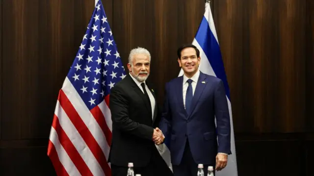 Marco Rubio shaking hands with  Yair Lapid in front of US and Israeli flags