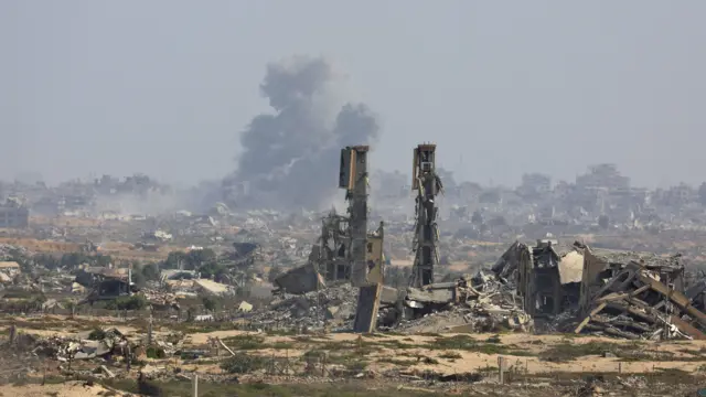 The remains of a building in Gaza stands among the debris of other buildings while a cloud of grey smoke billows in the background