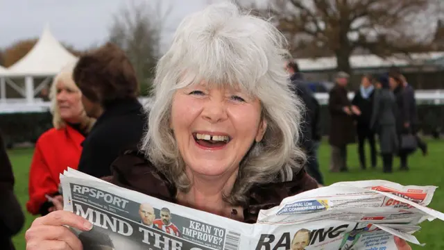 Jilly Cooper laughing while reading a newspaper