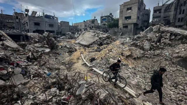 Rubble is seen in Gaza City, as Palestinians walk by buildings that have been reduced to nearly nothing