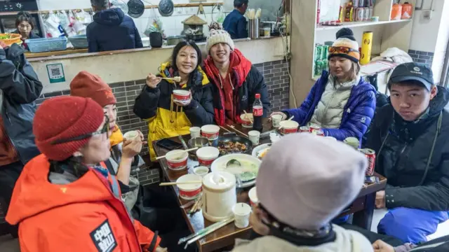 A group of hikers in winter wear sitting around a table eating