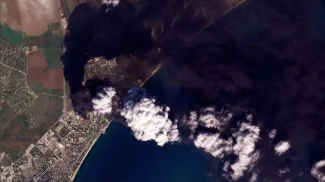 Satellite image of smoke rising into the air and drifting across a body of water
