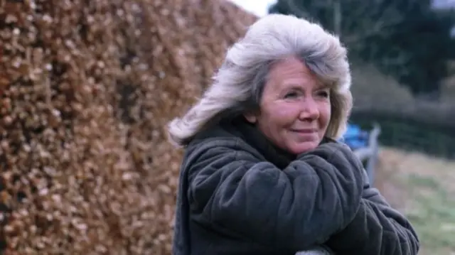 Jilly Cooper leans on a fence and smiles