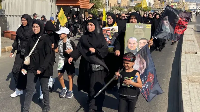 A group of woman and children hold flags and posters including the image of Hassan Nasrallah