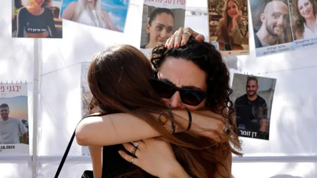 Two women hug with pictures of the victims of the attack hanging behind them