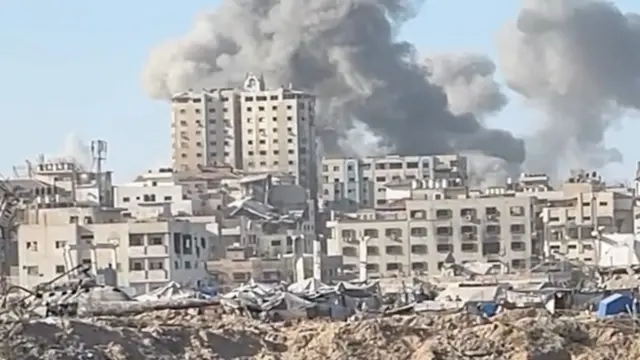 Two plumes of smoke seen rising over Gaza City, rubble and damaged buildings are visible in the foreground
