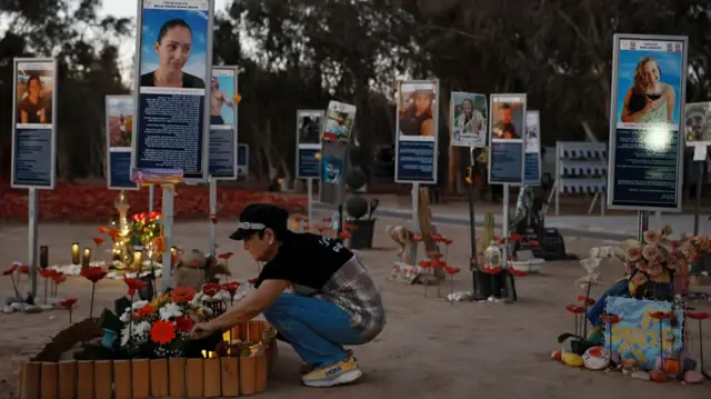 Woman tending to flowers by a placard with a picture of a victim of the 7 October 2023 attacks
