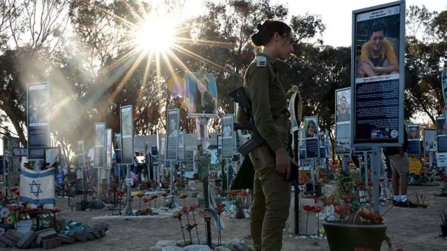 Uniformed woman stands in tribute in front of a placard with the picture of a victim of the 7 October attacks