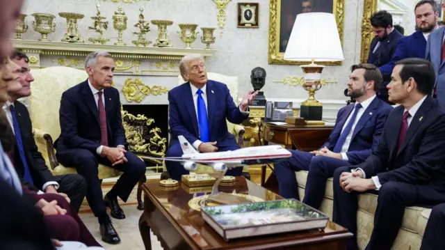 A wide shot of Carney and Trump sitting next to each other in the Oval Office, with other members of Trump's cabinet also present, including JD Vance and Marco Rubio