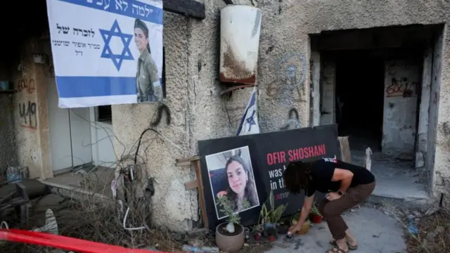 A member of the kibbutz community of Kfar Aza places a candle in front of a tribute for Ofir Shoshani
