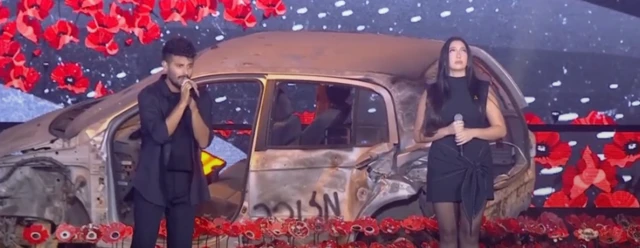Performers in front of burnt car