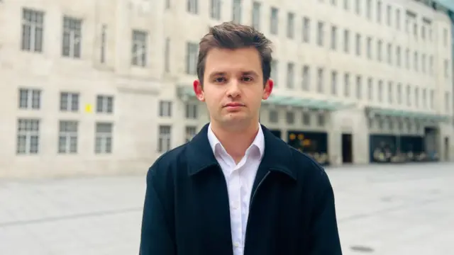 Louis Danker pictured wearing a white shirt and a black jacket.