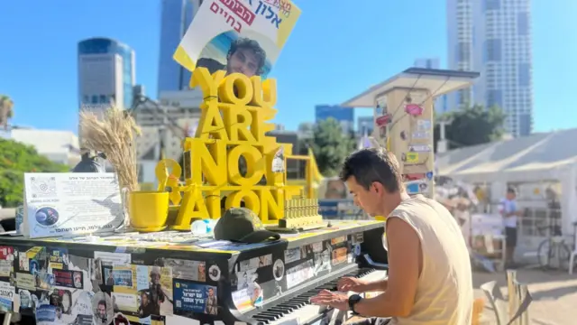 A man plays a piano outside - the instrument has a number of stickers and posters with photos of the victims