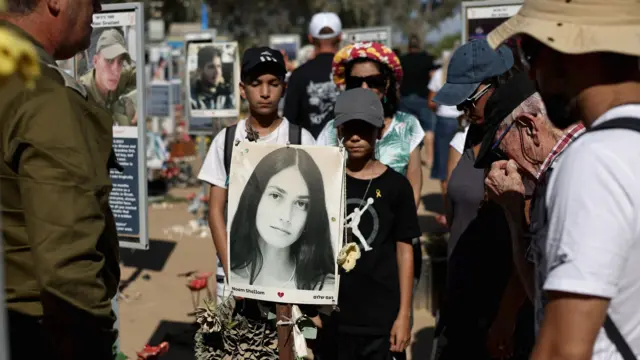 People gather at the site of the Nova music festival where photos of the victims stand