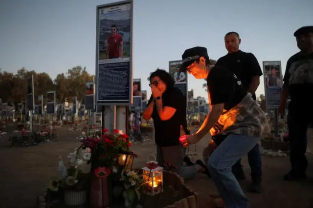A woman places a candle as people grieve at the site of the Nova festival where partygoers were killed and kidnapped