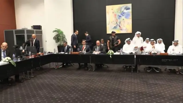 Israeli and Qatari officials sit and stand around long conference tables during Israel-Gaza peace talks