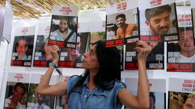 Einav Zangauker, mother of Matan, looks at a picture of her son that she's holding up in her left hand. In her right hand, she holds pictures of two other Israeli hostages in Gaza