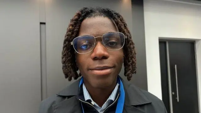 Augustus Roberts looks to camera. He is wearing a blue lanyard