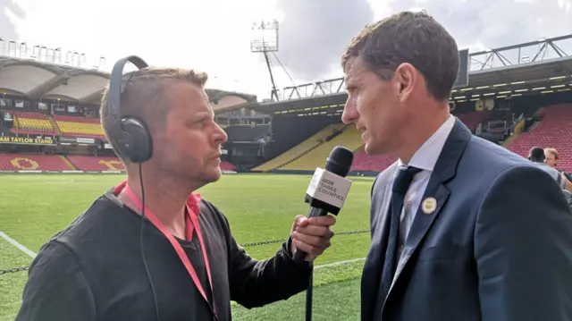Javi Gracia being interviewed at the side of the Vicarage Road pitch. The stadium is empty.