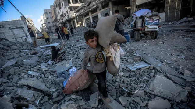 young child collects dusty pillows from rubble of buildings