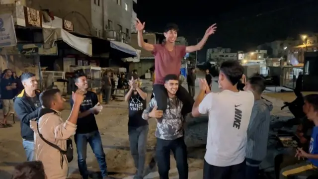 Group of young men with hands raised in celebration, with one man on the shoulders of another