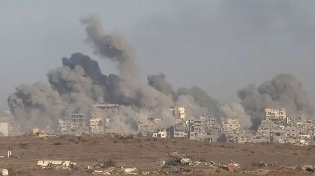 plumes of smoke rising over brown and grey buildings