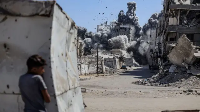 child hiding behind structure as smoke and explosions go off in background