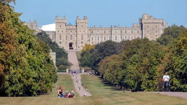 Windsor Castle surrounded by lawns and trees with people walking and picnicking