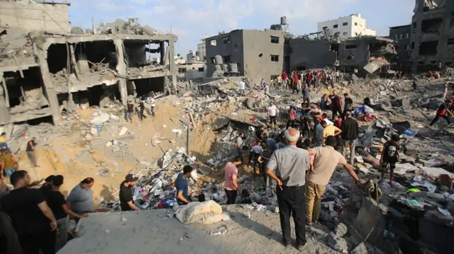 crowds of Palestinians stand around destroyed buildings