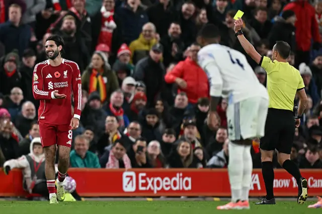 Referee Stuart Attwell (R) shows a yellow card to Liverpool's Hungarian midfielder #08 Dominik Szoboszlai