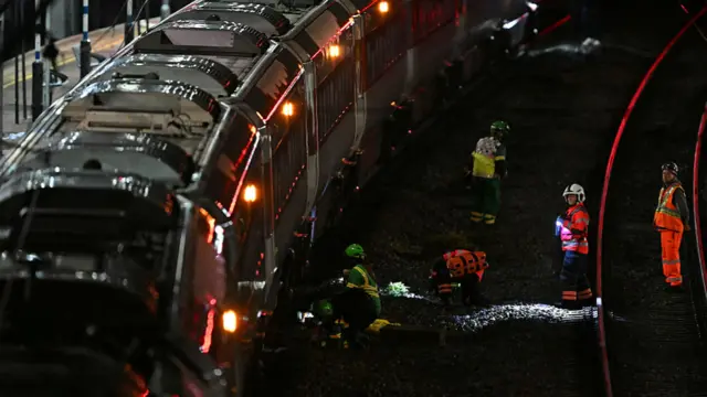 Police officers and members of the emergency services search the track beneath an LNER Azuma train at Huntingdon Station.