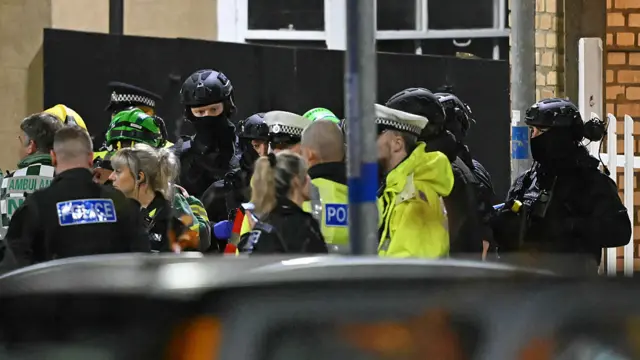 Armed Police officers stand with members of the emergency services outside Huntingdon Station.