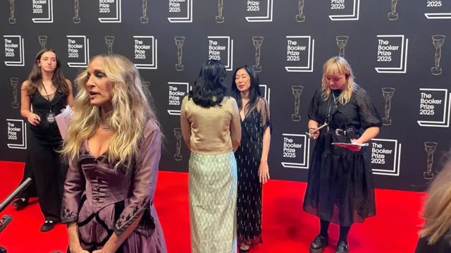Behind Sarah Jessica Parker, nominated authors Katie Kimatura and Kiran Desai have a catch-up on the red carpet