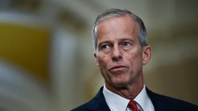 Senate Majority Leader John Thune wears a blue suit and red tie.