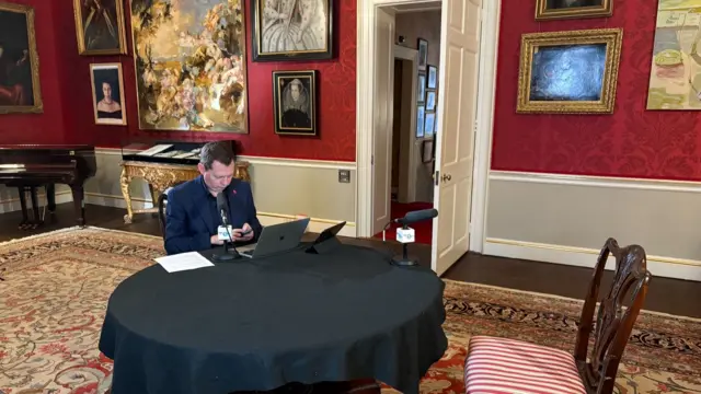 Wearing a dark navy suit inside the red walls of 11 Downing Street, Matt Chorely looks into a macbook laptop ahead of an interview with Rachel Reeves