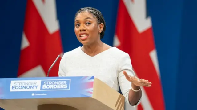 Badenoch speaking at podium in front of two Union Jack flags