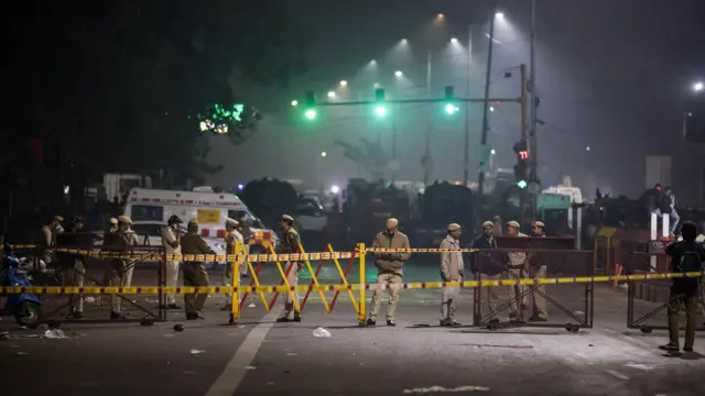 Emergency personnel work at the site of the explosion. Yellow and red police tape and temporary fencing has been put up and there are several men in uniform as well as an ambulance