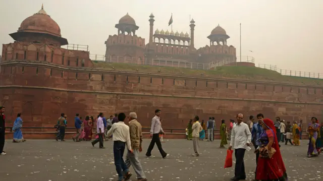 People walk in front of the Red Fort in Delhi. The Red Fort is an imposing building made of red brick with rounded minarets