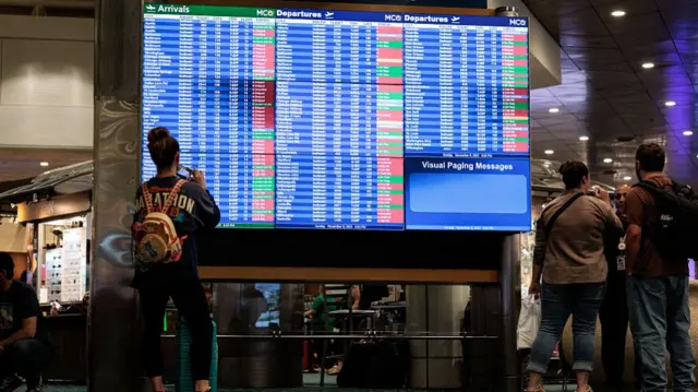 travellers look at giant board showing a majority of flights are delayed or cancelled