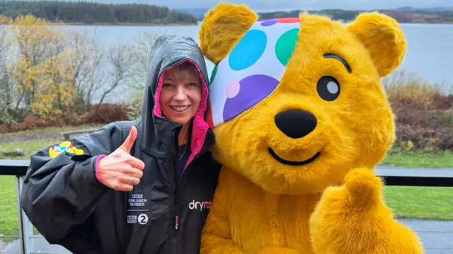 Sara Cox smiling next to Pudsey, both with their thumbs up
