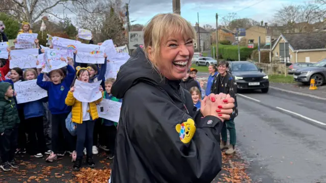 Sara smiles in front of a crowd of children with hand-made signs