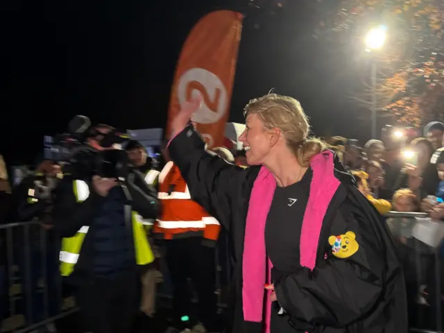 Sara Cox smiling and waving at the finish line for Day 2
