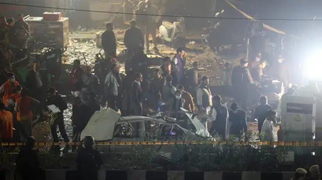 general The aftermath of an explosion in Delhi, showing a badly damaged car and several investigators in the vicinity