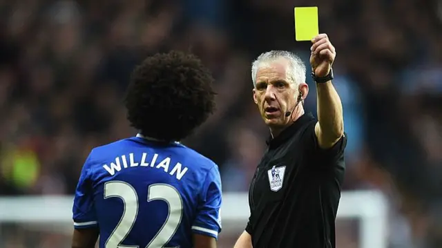 Referee Chris Foy shows a yellow card to Willian of Chelsea